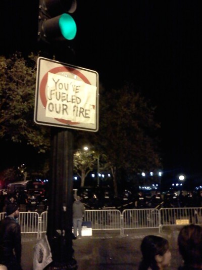 Sign says you've fueled our fire. Riot police stand behind