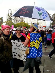 Wonder Woman protesting with umbrella that is painted with a flower and "They tried to bury us they didn't know we are seeds"