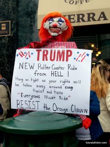 Clown puppet with sign: "TRUMP: New roller coaster ride from HELL! Hang on tight as your rights are stripped away at every twist and turn. Everyone must ride!"